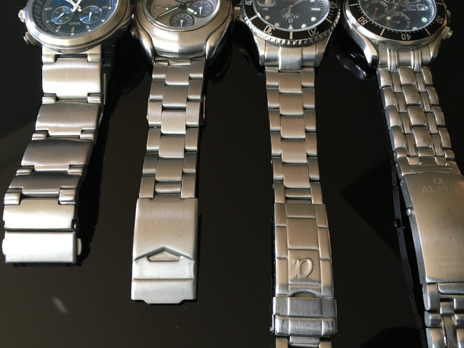 Four analog wristwatches on stainless steel bracelets lying side by side